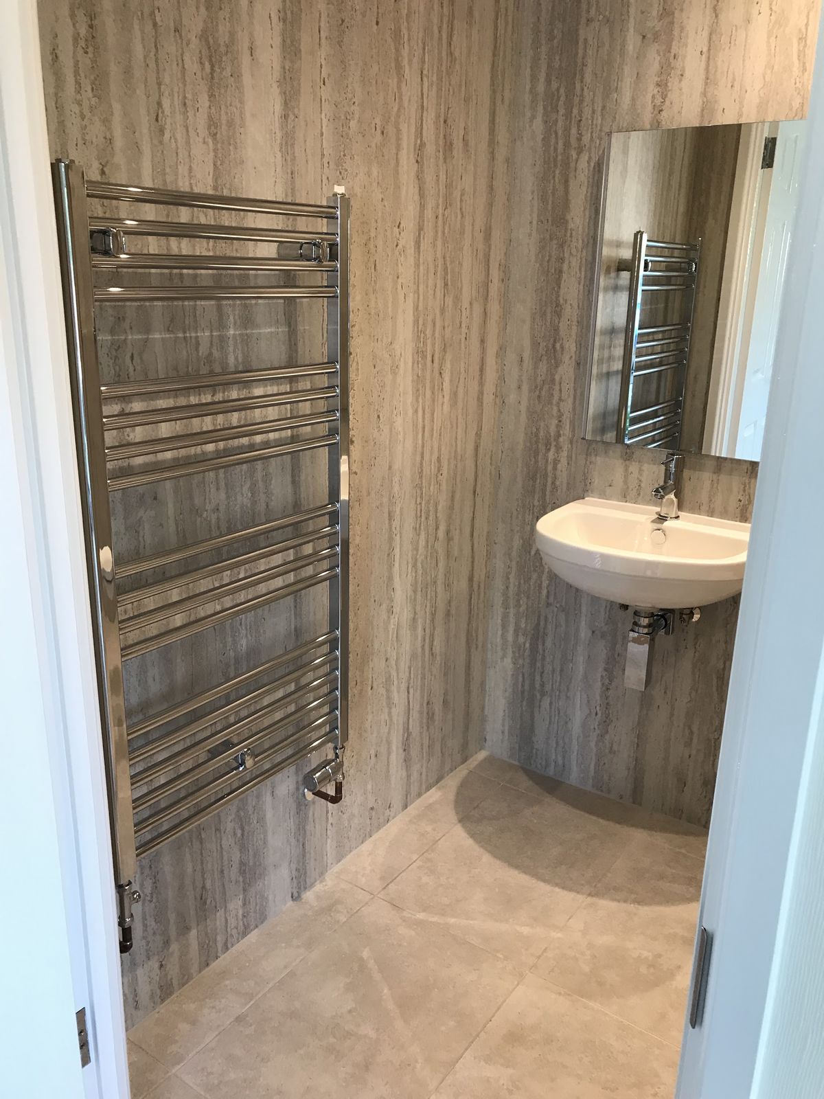 A finished shower room with a chrome towel radiator and a basin on stone-effect wall panels
