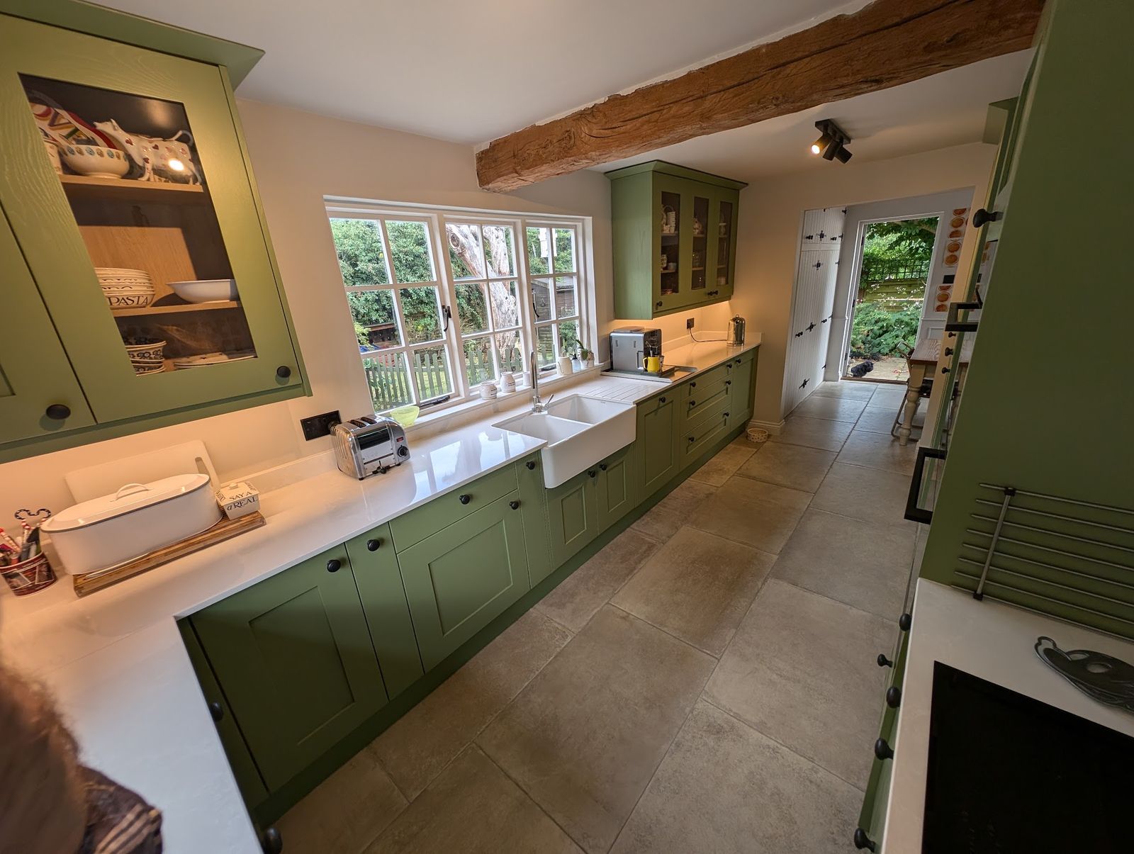 A sage green kitchen with a Belfast sink under a beamed ceiling