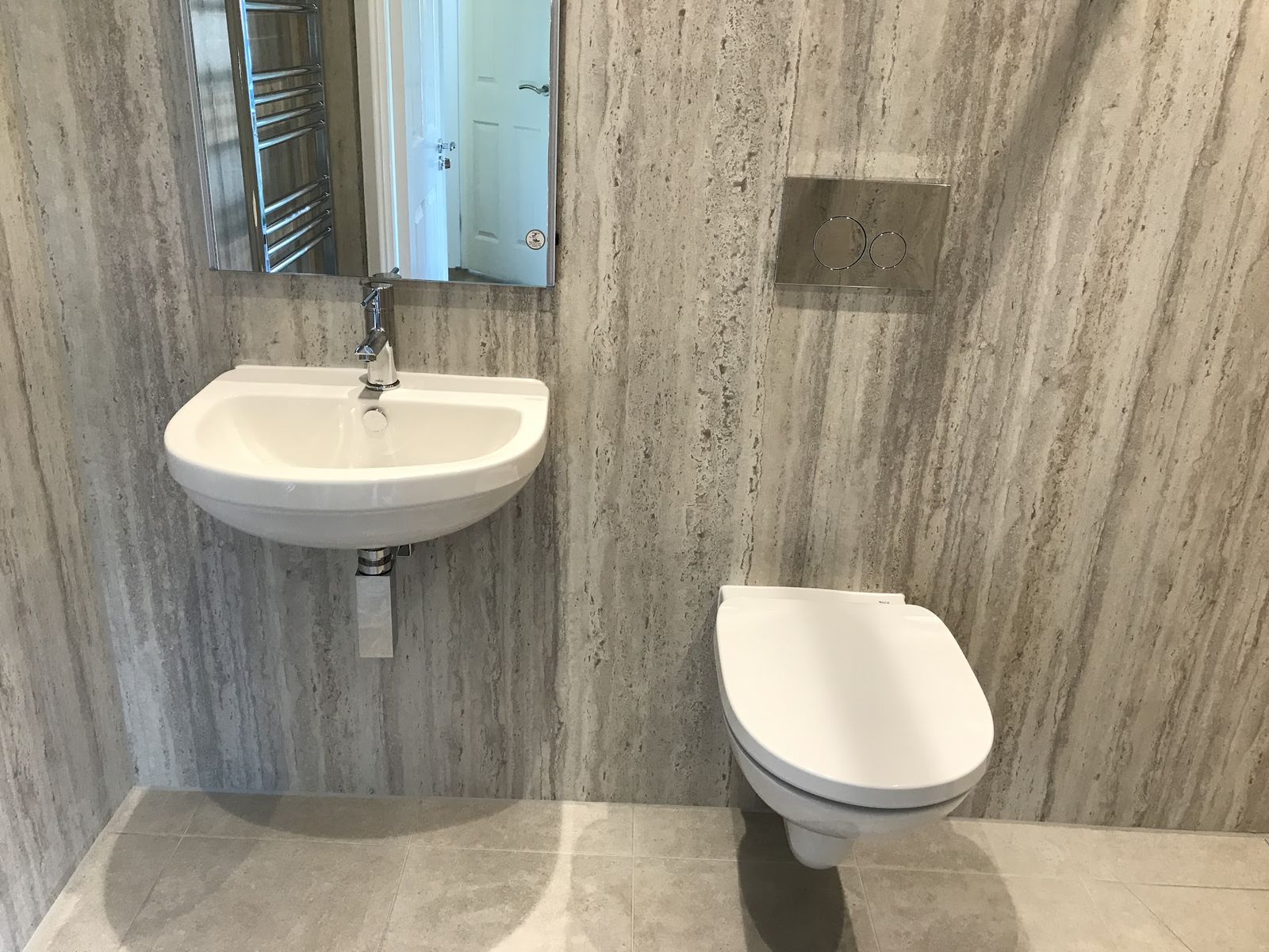 A wall-hung toilet, basin and flush plate on stone-effect wall panels