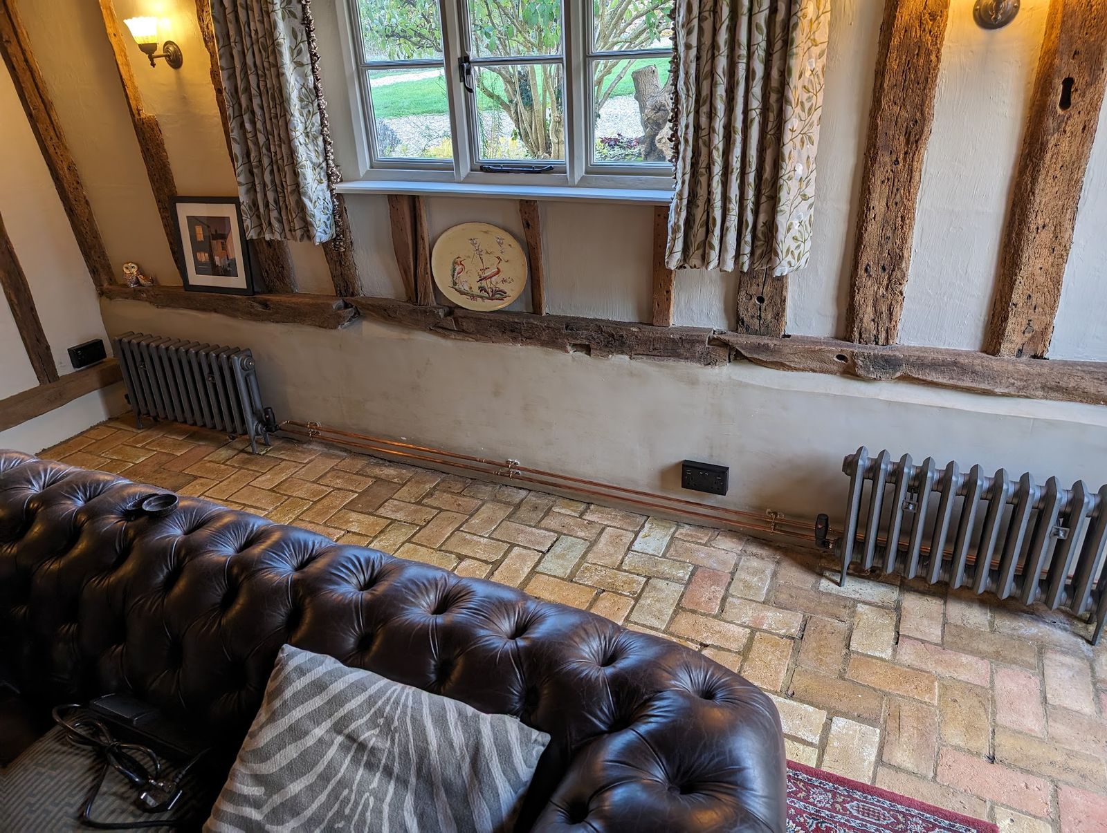 A beamed sitting room with two column radiators on a brick floor